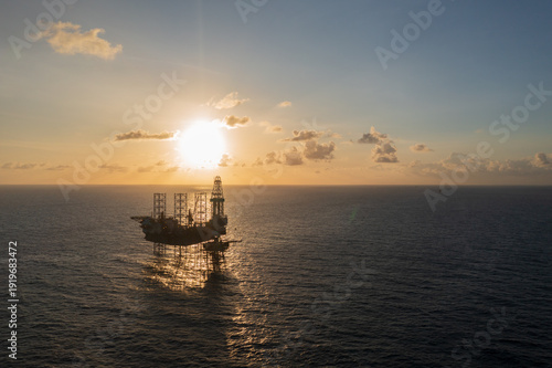 Aerial view from a drone of big jack up offshore drilling oil rig, production platform and supply vessel In the ocean during sunset - Oil and Gas Industry
