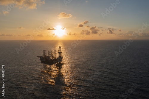 Aerial view from a drone of big jack up offshore drilling oil rig, production platform and supply vessel In the ocean during sunset - Oil and Gas Industry