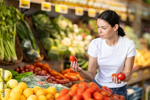 Foto Girl client near vegetable stand in store choose tomato