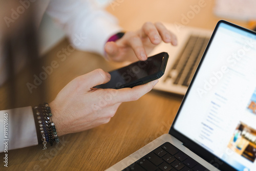 A person uses a smartphone and laptop to research travel options, browsing accommodation filters and booking details on a website.