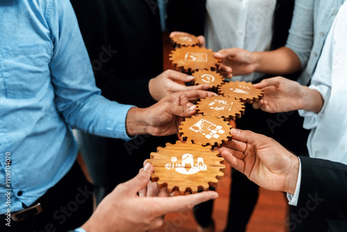 Quadro su tela A compelling visual of diverse hands holding wooden gears with business symbols, exemplifying teamwork and strategic planning in a corporate environment