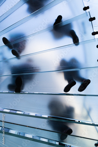Silhouettes of people walking on glass stairs in modern architecture