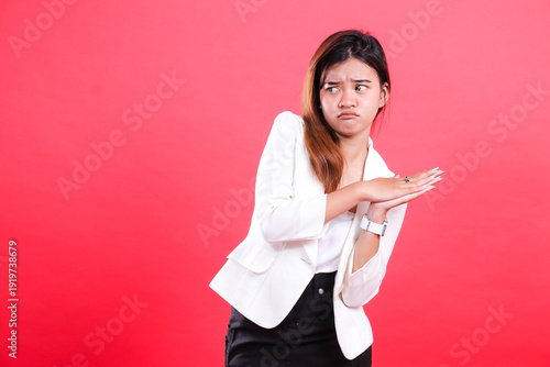 A woman with long brown hair wearing a white jacket, black shirt and black skirt is posing with clasped hands, isolated on a red background