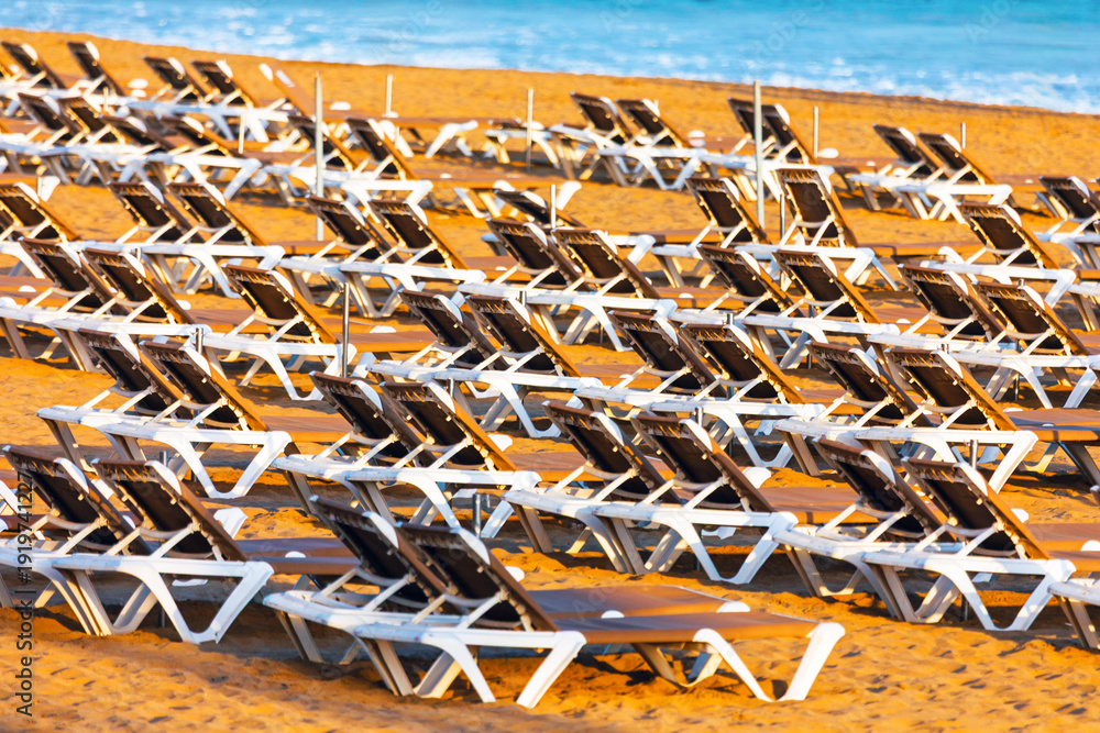 Φωτογραφία Rows of empty lounge chairs line a golden sandy beach, basking in warm sunlight near calm blue sea