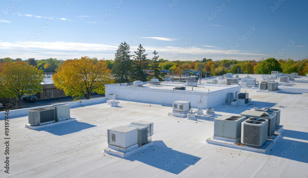 Obraz premium White flat roof with various air conditioning units and rooftop hvac systems in an urban setting