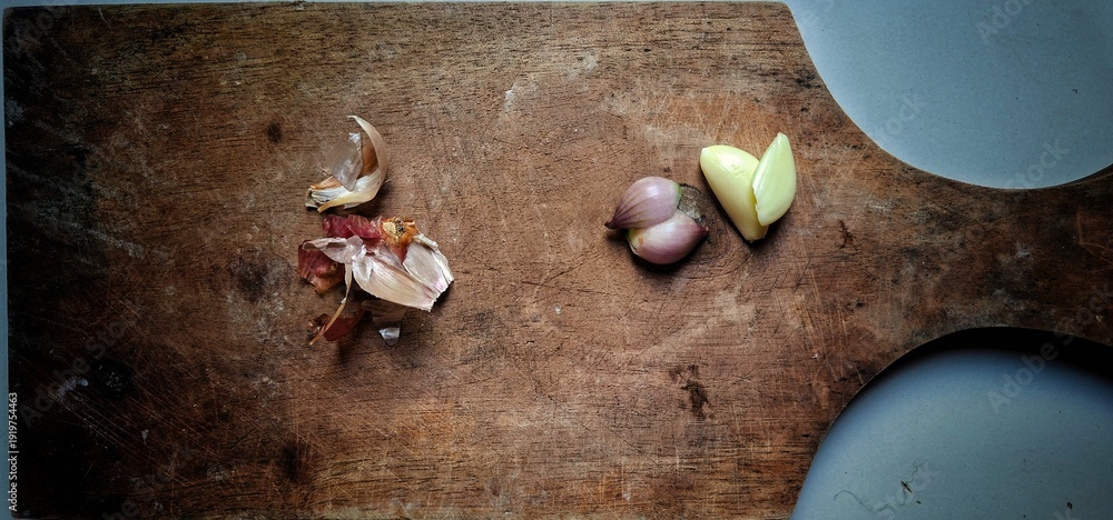 Εκτύπωση καμβά one clove of garlic and one clove of shallot on a wooden chopping board that looks worn from frequent use