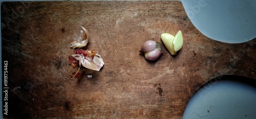 Foto one clove of garlic and one clove of shallot on a wooden chopping board that looks worn from frequent use