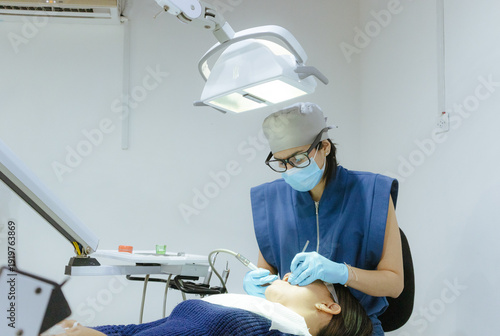 Dental professional, wearing mask and gloves, working on a patient's teeth in a brightly lit, sterile examination room