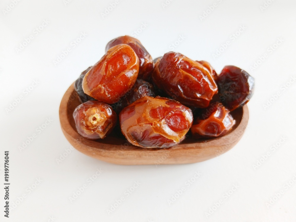Obraz premium Close up of premium dried dates in a wooden bowl placed on burlap fabric over white background with copy space. Minimalist food photography concept for Ramadan, Eid Mubarak, healthy snack, and Islamic