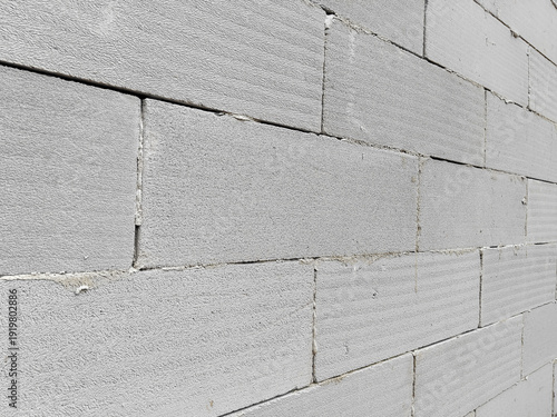 A white brick wall viewed at an angle, showing rough textured blocks, visible seams, and slight stains, creating a simple, solid, and structured architectural surface
