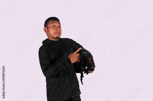 An Asian adult man wearing a black shirt smiles happily after getting a new idea, posing as he shows his idea to an empty space while holding a helmet.