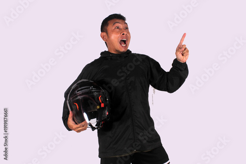 An Asian adult man wearing a black shirt smiles happily after getting a new idea, posing as he shows his idea to an empty space while holding a helmet.