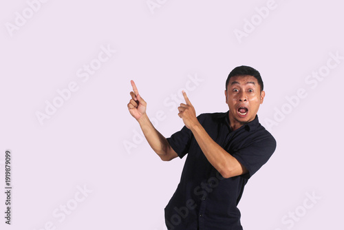 An Asian adult man wearing a black shirt smiles happily after getting a new idea, posing as he shows his idea to an empty space.
