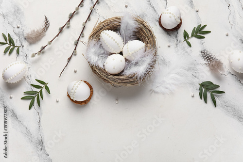 Easter eggs decorated with pearls and feathers in nest on marble background