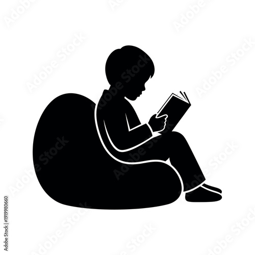 Silhouette of a young boy reading a book while sitting comfortably on a bean bag chair.