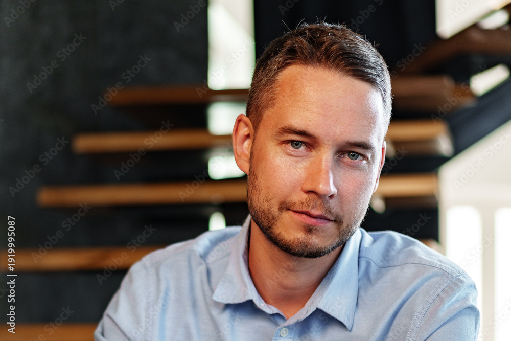 Obraz premium Man poses for a portrait indoors near wooden stair structure during a sunny day