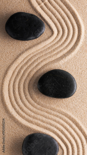 Quadro em tela Black stones placed on a textured sand surface with curved patterns in the backg