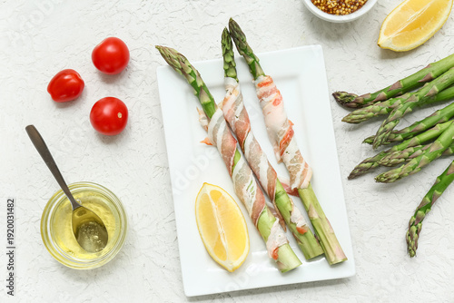 Plate of fresh green asparagus with bacon, lemon and cherry tomatoes on white background