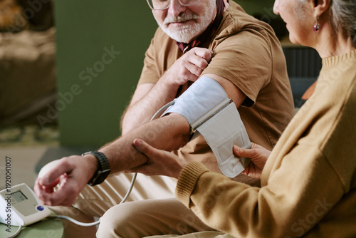 Φωτογραφία Senior Caucasian man sitting while senior Caucasian woman measuring blood pressu