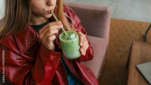 Fotografía Young woman in a red leather jacket drinks a refreshing iced matcha latte with a