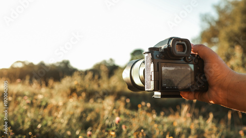 Hand holding a professional camera to capture the beauty of a sunlit meadow