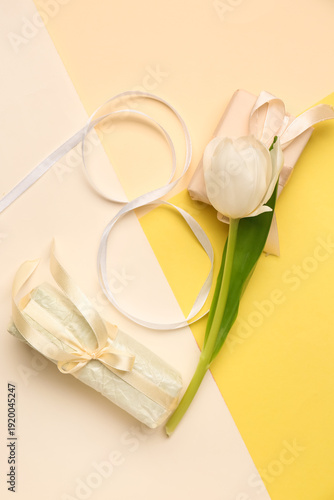 Figure 8 made of ribbon with gift box and beautiful tulip on colorful background. International Women's Day celebration