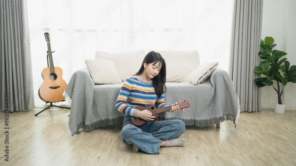 Fototapeta premium Young woman playing ukulele on living room floor, cozy atmosphere with plant and guitars, vibrant colors, relaxed setting, personal space, indoor lifestyle