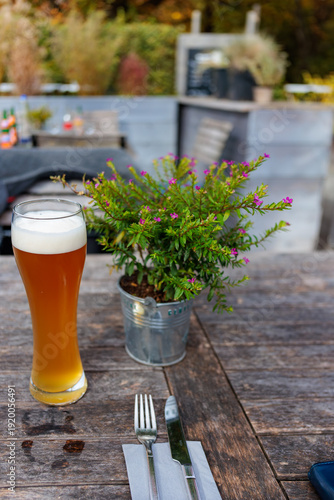 Tall wheat beer glass on rustic wooden table in outdoor garden restaurant