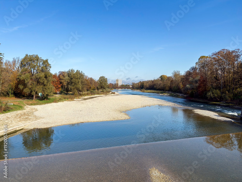 Wide river landscape with gravel banks and autumn trees under blue sky