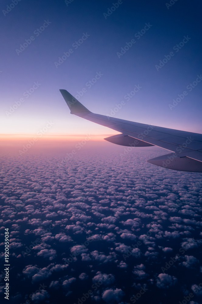 Fototapeta premium Airplane Wing Above Cloudscape at Sunrise – View from Window Seat