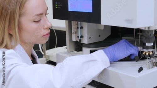 Blonde female scientist in lab coat loading sample vials into HPLC instrument. Analytical chemistry, pharmaceutical research and laboratory testing concept.