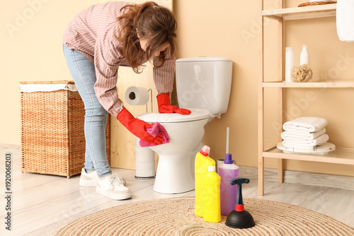 Young woman cleaning toilet...