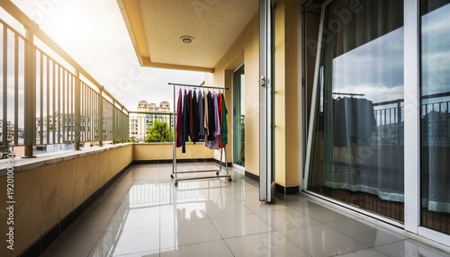 Modern apartment balcony featuring a laundry rack with hanging clothes. Bright outdoor terrace with a view of the city under a clear sky during laundry day.