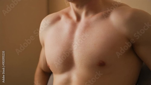 A shirtless man showcasing his toned physique in a warm-toned indoor setting