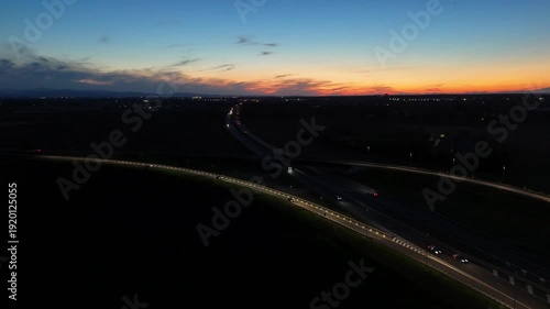 Aerial footage of a tall telecommunication tower equipped with antennas and satellite dishes, transmitting signals against a clear dark blue sky at dusk in a rural landscape
