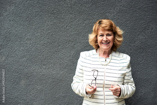 Portrait of smiling senior businesswoman against grey wall