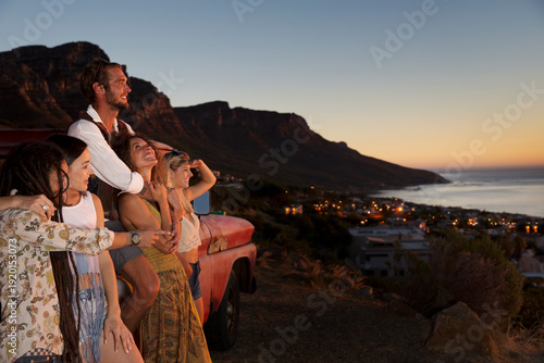 Young people outside pick up truck at the coast enjoying the sunset