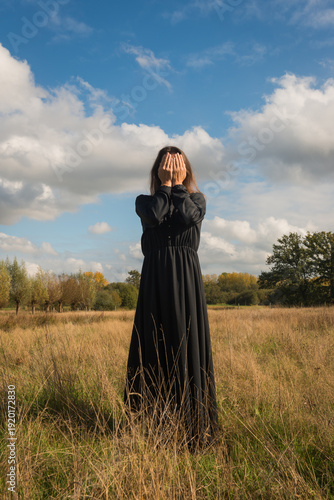 art portrait of woman in black classic dress in field veiled in autumn light