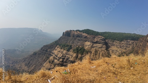 Scenic panoramic view of a rugged mountain cliff and deep valley under a clear blue sky in the Western Ghats, Maharashtra, India
