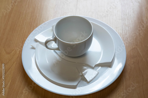Cup and plate broken on a wooden table after an accident during a meal