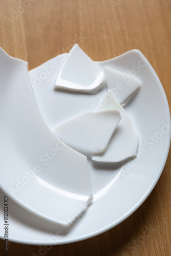 Broken pieces of white ceramic plate on wooden table show signs of damage and brokenness