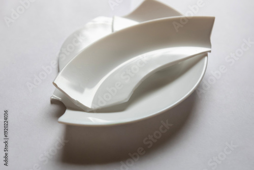 White ceramic plates stacked in a simple arrangement on a light surface, showing shapes and curves of the design