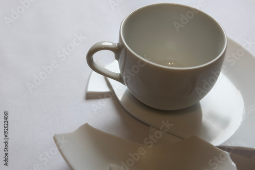 Cup and saucer on a white tablecloth with broken pieces nearby in a dining setting