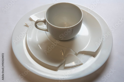 Broken cup and plate on a table after an accident in a kitchen during morning hours