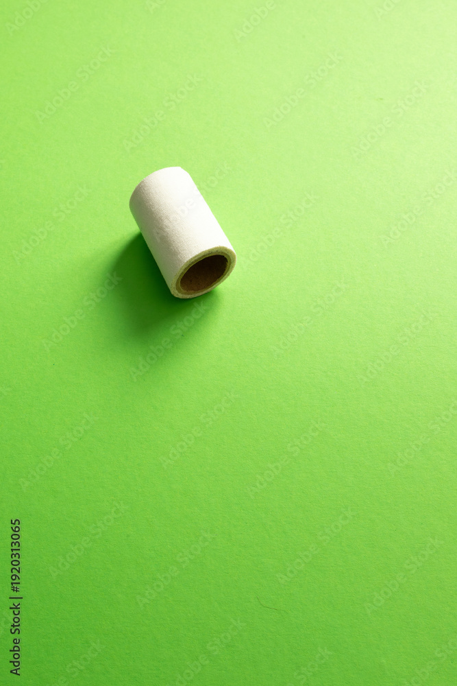 Obraz premium A white medical tape roll sits on a vibrant green surface with ample negative space. A minimalist composition focusing on medical supplies and first aid care. vertical