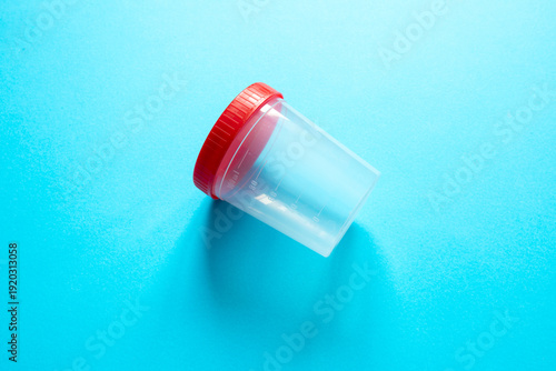 Canvastavla empty, transparent plastic specimen container with red screw-cap lies diagonally at the center of a solid, vibrant blue background