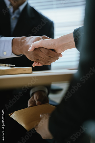Close-up of hands exchanging a sealed envelope filled with cash under a desk, symbolizing bribery, corruption, illegal transaction, and unethical business practice.