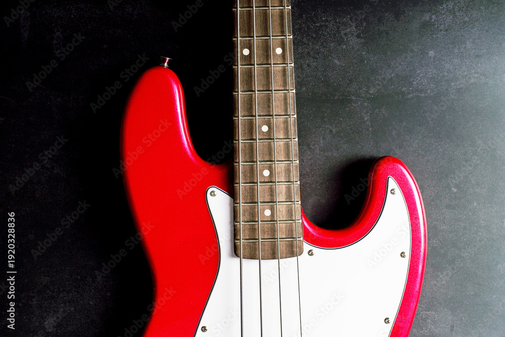 Obraz premium Detail of a red electric bass guitar with visible fretboard and headstock on neutral textured background. Music instrument concept, rock and funk sound, studio close up. 