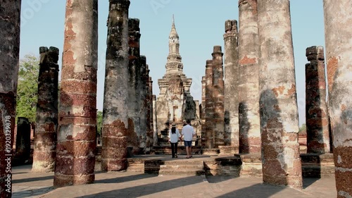 Travelers stroll through the stunning ruins of Sukhothai Historical Park, surrounded by tall ancient columns and historic structures, capturing the essence of Thailand rich heritage and tranquility.