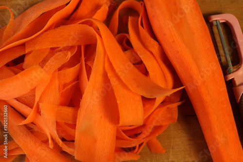 Photos Carrot peels and a peeler on a wooden cutting board in a kitchen setting during